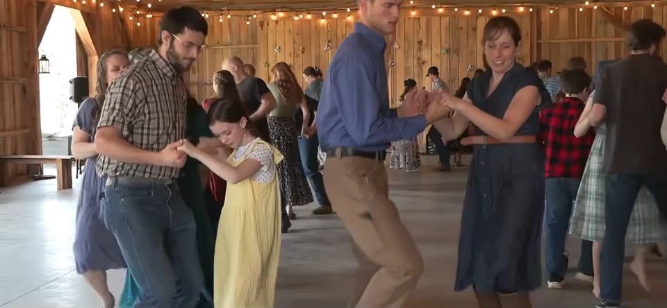 Adults and children laughing while dancing in pairs inside the barn